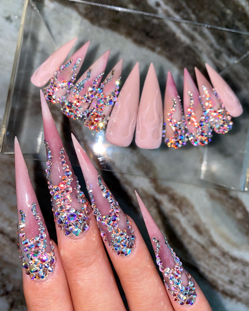 Four fingers with long, pointed, pink nails, and flames made of crystal on top.  A full set of nails with the same design are displayed in the background